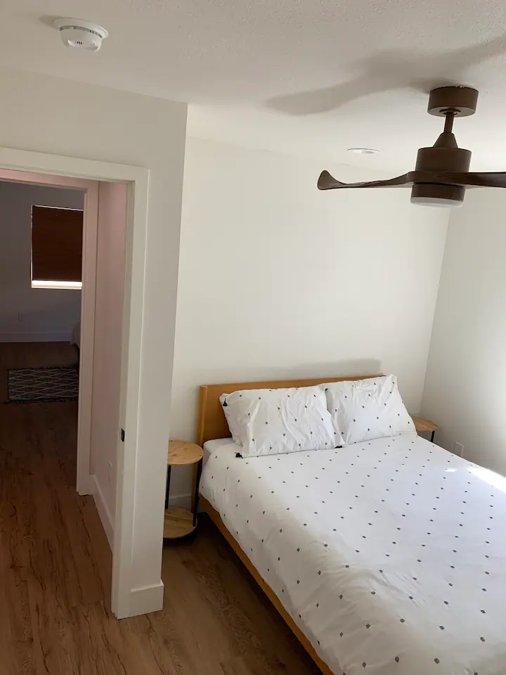 A bedroom with a bed, ceiling fan and hardwood floors.