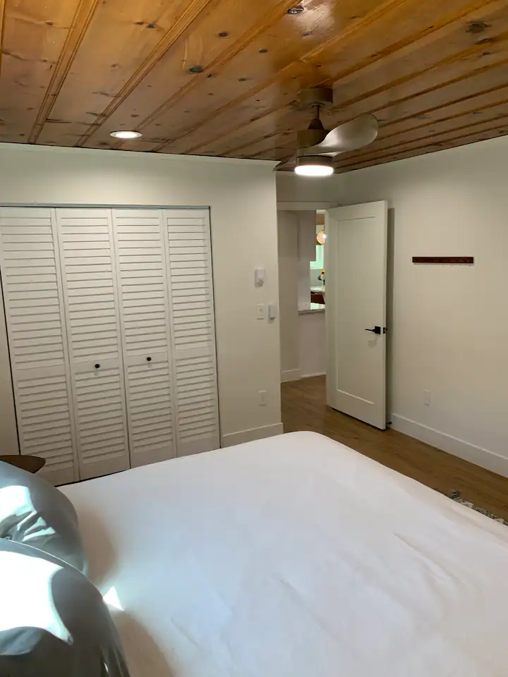 A bedroom with white walls and wooden ceiling.