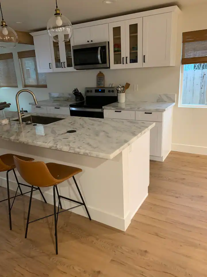 A kitchen with white cabinets and wood floors.