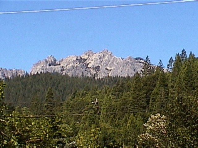 A mountain with trees in the foreground and power lines overhead.