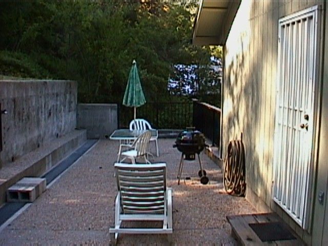 A patio with an umbrella and chairs on the ground.